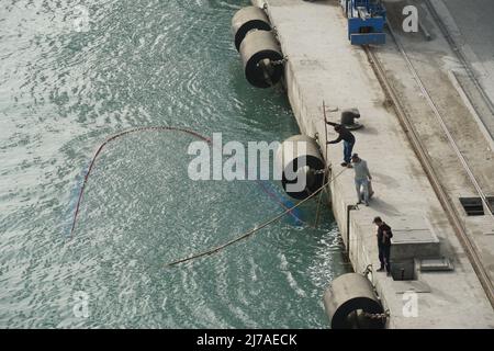 Gruppe von drei Fischern fangen Fische mit einem Netz im Hafen von Damietta, Ägypten im Container-Terminal. Sie bewegen sich am Pier entlang. Stockfoto