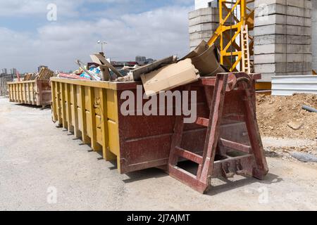 Riesiger Haufen auf Metall großer, überladener Müllcontainer, gefüllt mit Bauabfällen, Trockenbau und anderen Schutt in der Nähe einer Baustelle. Stockfoto