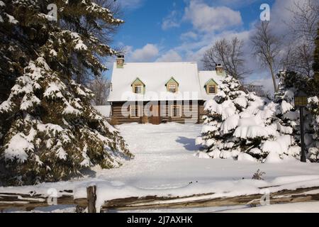 Altes Blockhaus im kanadischen Stil aus dem Jahr 1800s, das im Winter durch einen rustikalen Holzzäunung geschützt ist. Stockfoto