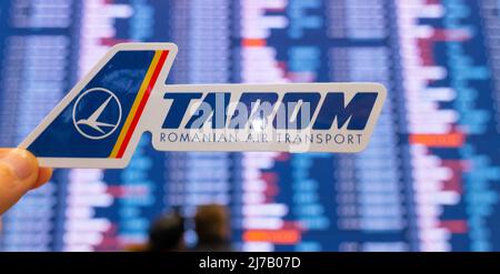 11. Dezember 2021, Bukarest, Rumänien. Das Emblem der Fluggesellschaft TAROM vor dem Hintergrund einer elektronischen Tafel mit einem Flugplan auf der int Stockfoto