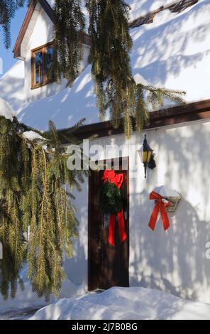 Vor der Tür aus braunem Holz befindet sich ein Haus im alten kanadischen Stil, das im Winter mit Weihnachtskränzen dekoriert ist. Stockfoto