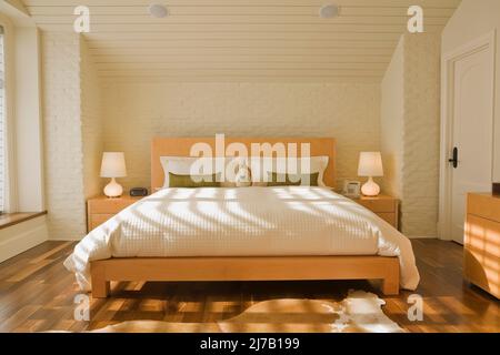 King-Size-Holzbett und passende Beistelltische im Hauptschlafzimmer im luxuriösen Zuhause. Stockfoto