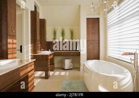 Modern sein und ihr eigenes Badezimmer mit braunen hölzernen Eitelkeiten und freistehender ovaler Badewanne im luxuriösen Zuhause. Stockfoto