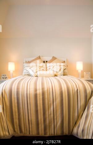 Doppelbett bedeckt mit gestreifter Bettdecke im Gästeschlafzimmer im luxuriösen Haus. Stockfoto