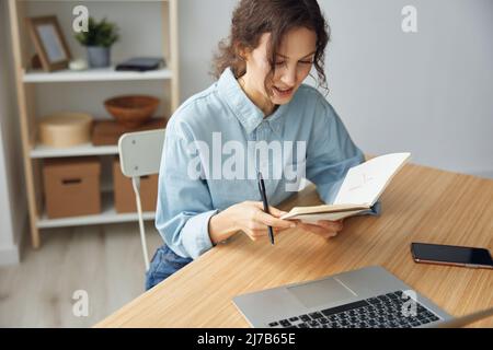 Draufsicht Aufnahme von nachdenklichen glücklich liebenswert fröhlich niedlichen Geschäftsfrau im Heimbüro lesen ihre To-do-Liste Pläne auf Notebook sitzen am Tisch mit trendy Stockfoto