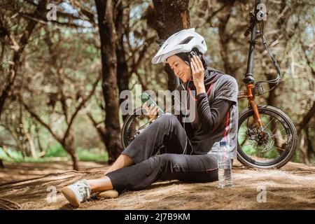 Verschleierte Mädchen lächelnd tragen Kopfhörer, während sitzen ruhen, während Radfahren Stockfoto