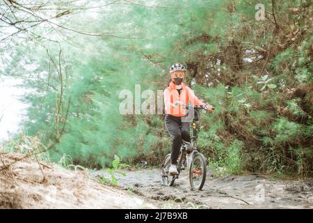 asiatische verschleierte Mädchen in schwarzer Maske Radfahren durch sandige Strecke Stockfoto