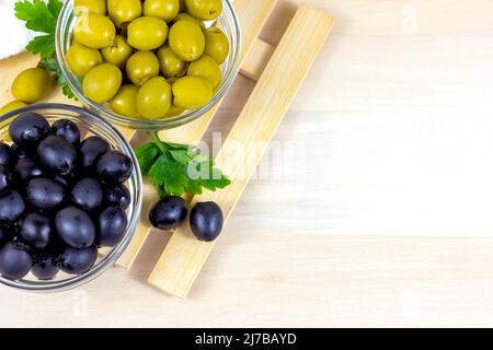 Viele grüne und schwarze marinierte ganze Oliven in der Glasschale mit Kopierplatz auf hellem Holzbrett Hintergrund in der Küche Draufsicht. Stockfoto