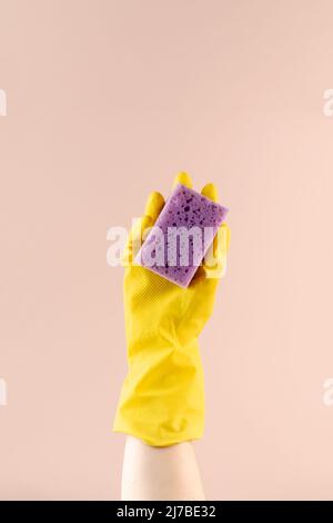 Hand in gelbem Handschuh hält Schwamm zum Spülen auf beigefarbenem Closeup-Kopierraum Stockfoto