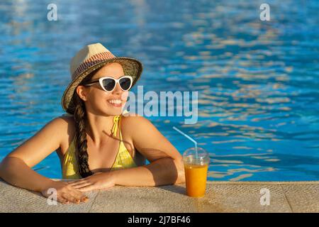 Lächelnde Frau, die im Swimmingpool Smoothies trinkt Stockfoto