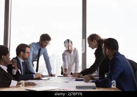 Selbstbewusster indischer Geschäftsleiter und vielfältiges Team, das Papierberichte diskutiert Stockfoto