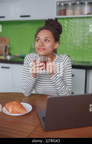 Porträt einer verträumten glücklichen Frau, die eine Tasse Tee in der Küche am Tisch hält Stockfoto