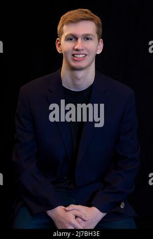 Schöner, braunes Haar junger Teen trägt einen isolierten schwarzen Hintergrund mit Sportmantel Stockfoto