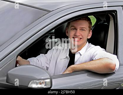 Schöner junger Mann mit riesigem Lächeln von seinem grauen Auto Stockfoto