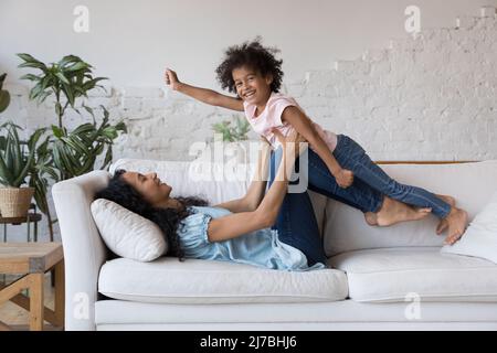 Glücklich afrikanische Mutter heben freudige Tochter Mädchen in der Luft Stockfoto