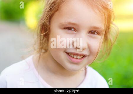 Glückliche kleine kaukasische Mädchen zeigen Vorderzähne mit großem Lächeln und gesundem Lachen auf dem Hintergrund der Natur am Sommertag. Glücklich lustig lächelndes Gesicht von jungen liebenswert schöne Frau Kind. Stockfoto