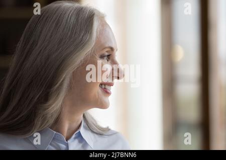 Glückliche, hübsche, reife Frau, die aus dem Fenster schaut Stockfoto