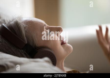 Fröhliche, ruhige Senior-Dame mit Kopfhörern, die Musik hört Stockfoto