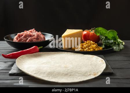 Pita mit Gemüse und Fleisch auf schwarzem Hintergrund. Kochvorgang Stockfoto