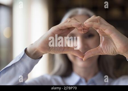 Ältere Frau zeigt Finger herzförmige Hände im Fokus Stockfoto