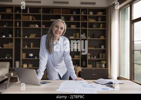 Glückliche, reife Geschäftsführerin, Frau, die bei statistischen Berichten auf Papier steht Stockfoto