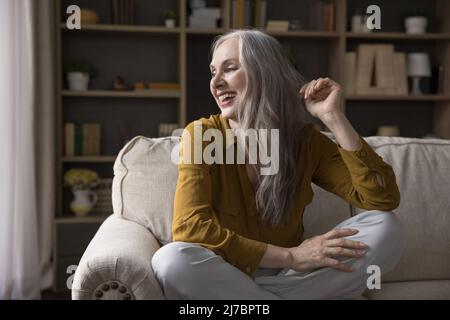 Fröhliche reife 50s Frau sitzt auf der Couch zu Hause Stockfoto