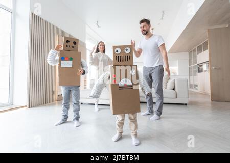 Fröhliche Familie von Eltern und zwei Kindern, die zu Hause tanzen wie Roboter, Kinder tragen handgefertigte Moving-Box-Kostüme aus Pappe Stockfoto