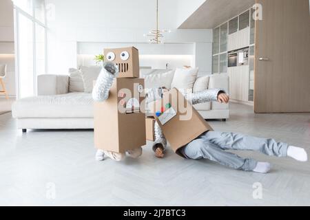 Glückliche zwei Kinder spielen Roboter zu Hause, Kinder tragen handgemachte Moving Box Kostüm aus Pappe Stockfoto