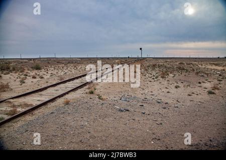 Verlassene Eisenbahnlinie in der Wüste. Verrostete Schienen und hölzerne Schabeln. Ampel am Horizont. Grau wolkig Himmel und Sonne. Stockfoto