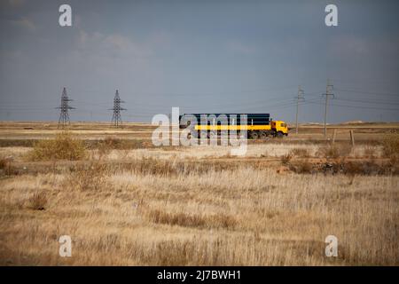 Transport von Kunststoffrohren mit großem Durchmesser auf einem gelben LKW. Gelbes trockenes Gras in der Steppe. Grauer Himmel. Stockfoto