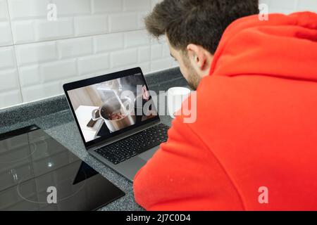Rezept, junge Mann lehnt sich auf Küchentisch beobachten Rezept, auf der Suche nach dem perfekten Weg für Huhn und Pasta Stockfoto