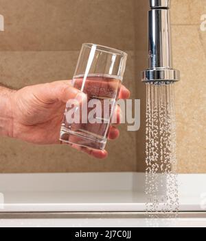 Mann, der ein Glas Wasser aus einem Wasserhahn bekommt Stockfoto