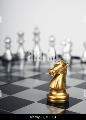 Das goldene Pferd, Ritterschach steht vor silbernen Schachfiguren auf Schachbrett auf weißem Hintergrund, vertikaler Stil. Führung, Kämpfer, sur Stockfoto