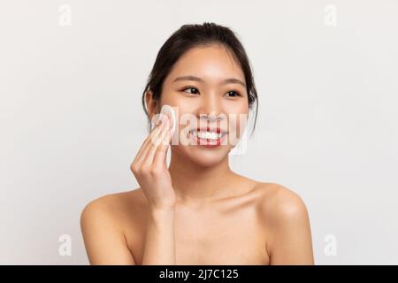 Junge asiatische Frau, die ihr Gesicht mit Wattepads putzt Stockfoto
