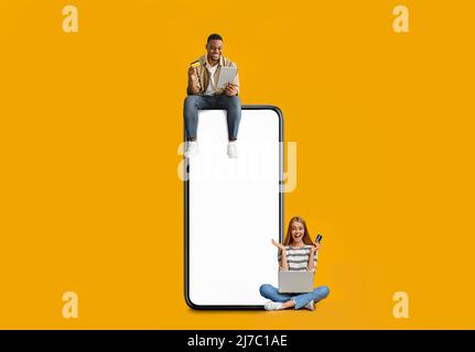 Paar sitzt auf weißem leeren Smartphone-Bildschirm und verwendet Geräte Stockfoto