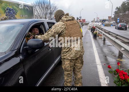 BROVARY, UKRAINE 08. März. Ein Mitglied des ukrainischen Militärs übergibt einem Fahrer zum Internationalen Frauentag an einem Kontrollpunkt in der Nähe der Stadt Brovary außerhalb von Kiew, während der russischen Invasion der Ukraine am 08. März 2022 in Brovary, Ukraine, eine rote Rosenblume. Russland begann eine militärische Invasion der Ukraine, nachdem das russische parlament Verträge mit zwei abtrünnigen Regionen in der Ostukraine gebilligt hatte. Es ist der größte militärische Konflikt in Europa seit dem Zweiten Weltkrieg Stockfoto