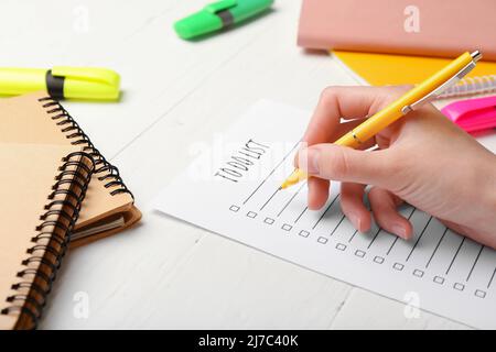 Frau, die eine To-Do-Liste auf weißem Holzhintergrund erstellt, Nahaufnahme Stockfoto