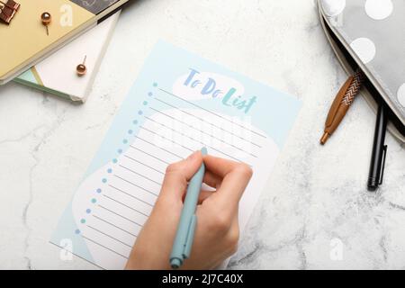 Weibliche Hand mit To-Do-Liste und Papeterie auf hellem Hintergrund, Nahaufnahme Stockfoto