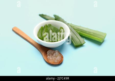 In Scheiben geschnittene Aloe-Pflanzenblätter in Schale und Holzlöffel mit Gel auf farbigem Hintergrund Stockfoto