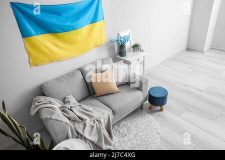Interieur des hellen Wohnzimmers mit hängender ukrainischer Flagge, Sofa und Tisch Stockfoto