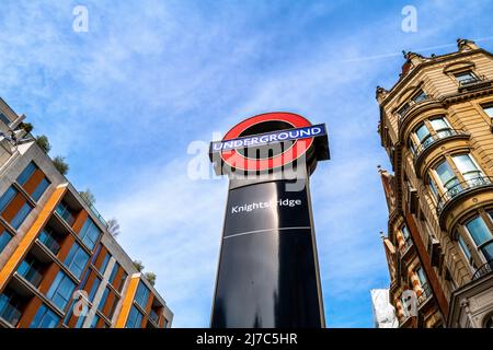 London, Großbritannien - 17. April 2022: Das U-Bahnschild Knightbridge, außerhalb des Eingangs zu Harrods, an der Brompton Road, London. Frühlingstag mit Blau Stockfoto