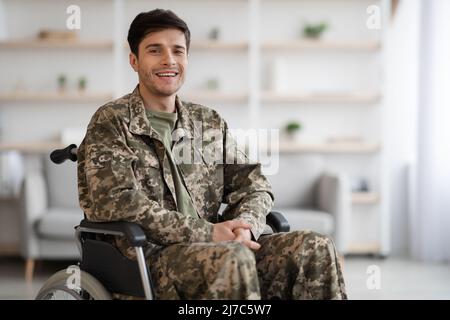 Glücklicher junger Mann Soldat im Rollstuhl sitzend, häusliche Innenausstattung Stockfoto