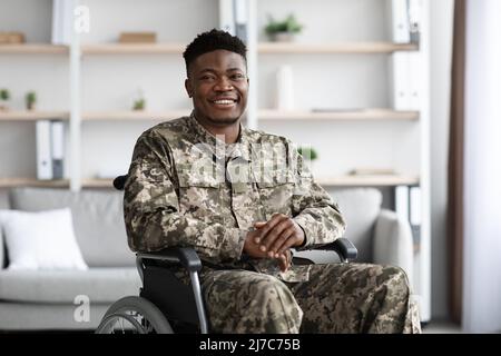 Positiver afroamerikanischer Militärangehöriger im Rollstuhl sitzend, Klinikinnenraum Stockfoto