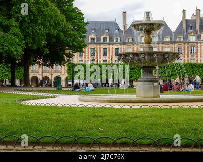 Gruppen von Menschen sitzen auf dem Rasen und genießen das Maiwetter auf dem Place des Vosges, Paris, Frankreich. Stockfoto