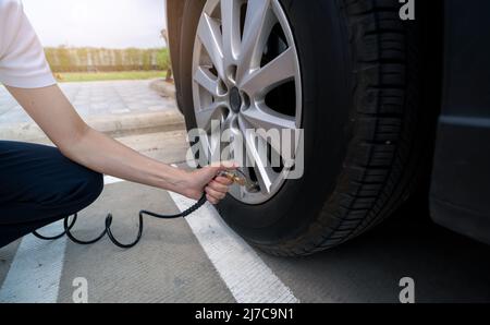 Frau bläst den Reifen auf. Frau, die den Reifendruck überprüft und Luft in den Reifen des Autorads pumpt. Autowartung zur Sicherheit vor der Reise. Stockfoto