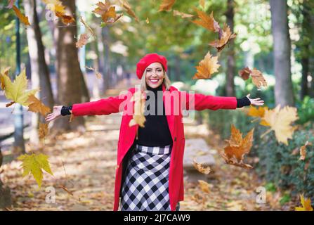 Fröhliche Frau, die Ahornblätter in die Luft wirft Stockfoto