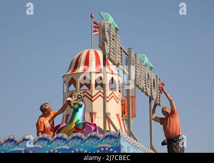 John-Henry Roper (links) und Kevin Morris polieren den Seedrachen unter blauem Himmel auf dem Messegelände an einem sonnigen Morgen in Hunstanton, Norfolk, Großbritannien, am 5. Mai 2022. Stockfoto