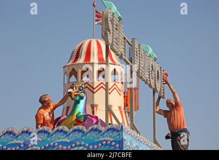 John-Henry Roper (links) und Kevin Morris polieren den Seedrachen unter blauem Himmel auf dem Messegelände an einem sonnigen Morgen in Hunstanton, Norfolk, Großbritannien, am 5. Mai 2022. Stockfoto