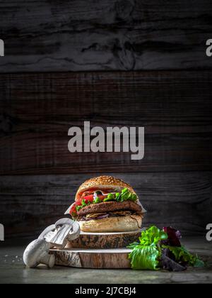 Hamburger mit Kichererbsen-Patty, Tomaten, Pilzen und Gemüse auf Roggenbrot. Herum, Pilze und Salat. Speicherplatz kopieren. Vertikale Aufnahme Stockfoto