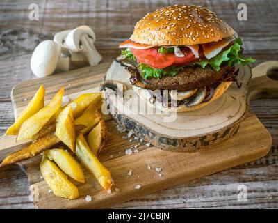 Hamburger mit Kichererbsen-Patty, Tomaten, Pilzen und Gemüse auf Roggenbrot. Um, Pommes und Pilze. Speicherplatz kopieren. Horizontale Aufnahme. Stockfoto